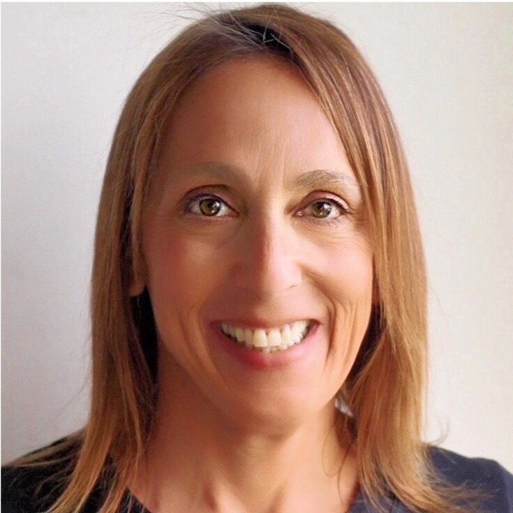 A woman with straight, shoulder-length light brown hair smiles at the camera. She is wearing a dark-colored top and is posed against a plain, light background.