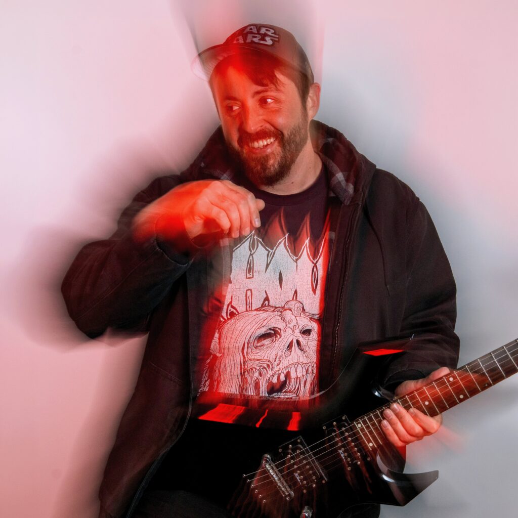 A man wearing a Star Wars cap and a black hoodie holds an electric guitar, smiling. Red light and motion blur effects, reminiscent of Elaine N’s dynamic style, create an energetic atmosphere.